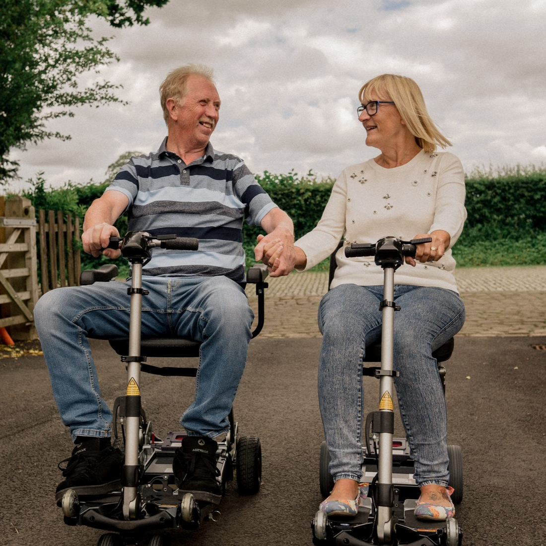 Two people using mobility scooters outdoors on a cloudy day.